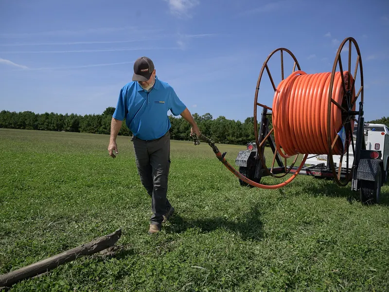 Worker pulling conduit from a large reel trailer on a utility installation site