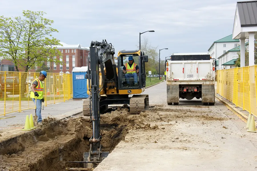Excavator and dump truck working an open utility trench along a city street
